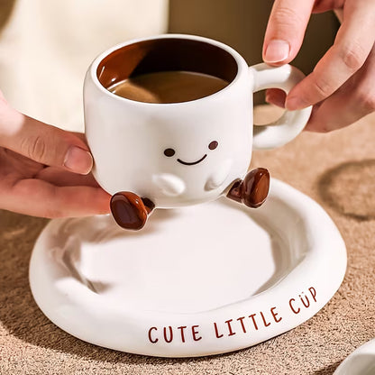 Cute white cup with smiling face design on a matching saucer, held by hands.