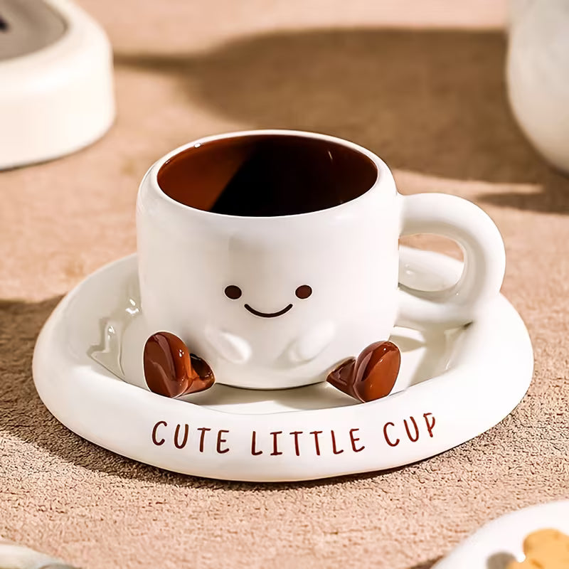 Cute white mug with smiling face design on a matching saucer, filled with coffee.