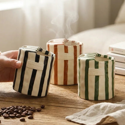 Striped ceramic pots on a wooden surface with a hand holding one pot, coffee beans, and books in the background.